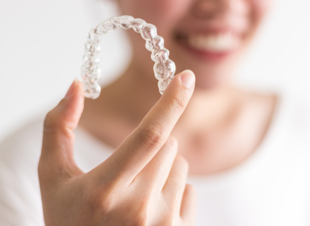 Mujer sonriente con funda de ortodoncia invisible en la mano